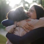 two women hugging each other while a sun glare is behind them