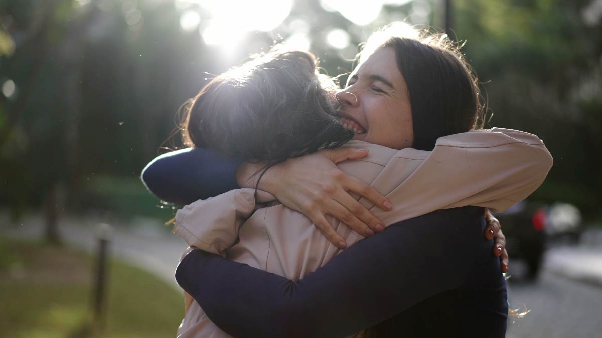 two women hugging each other while a sun glare is behind them